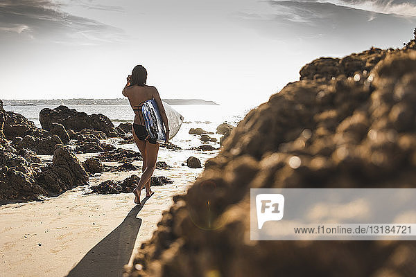 France  Brittany  young woman carrying surfboard on a rocky beach at the sea