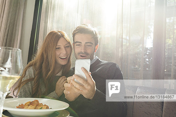Glückliches Paar betrachtet Handy in einem Restaurant