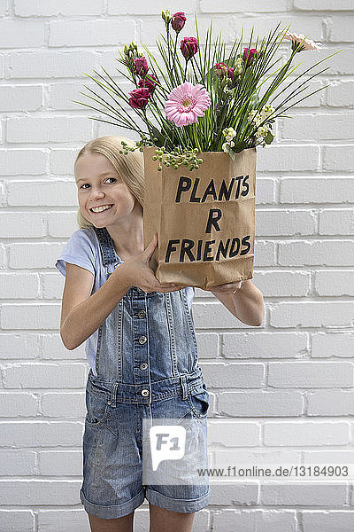 Portrait of smiling girl holding paper bag with flowers