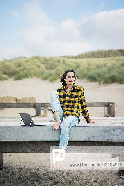 Reife Frau sitzt am Strand auf der Strandpromenade und benutzt einen Laptop