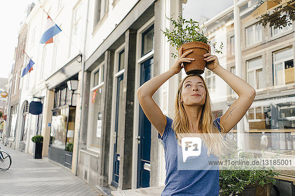 Niederlande  Maastricht  junge Frau  die in der Stadt einen Blumentopf auf dem Kopf balanciert