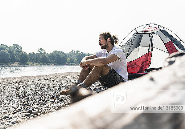 Junger Mann sitzt in einem Zelt am Flussufer