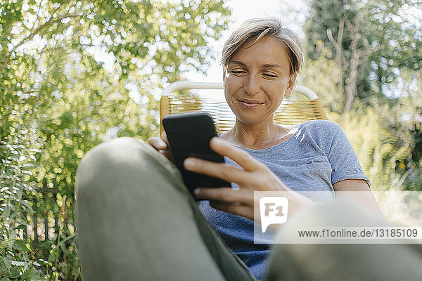Frau sitzt im Garten auf Stuhl und benutzt Mobiltelefon