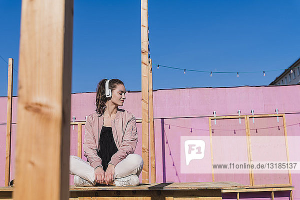 Entspannte junge Frau sitzt auf dem Bahnsteig und hört Musik