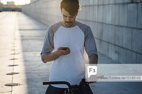 Junger Mann mit Pendler-Fixie-Fahrrad schaut auf Handy