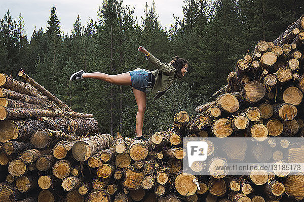 Junge Frau steht auf einem Bein auf einem Holzstapel
