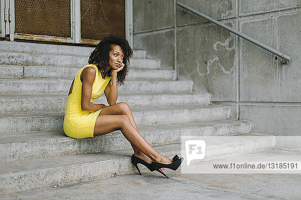 Fashionable businesswoman in yellow dress and high heels sitting on stairs