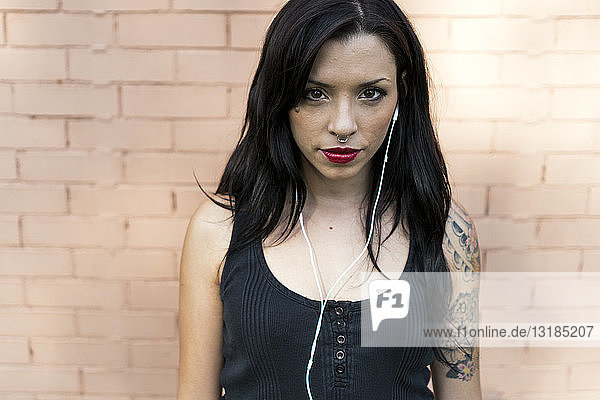 Portrait of young woman with nose piercing and tatoo using earphones