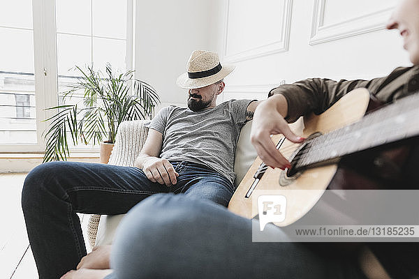 Relaxed couple sitting on couch  woman playing the guitar at home