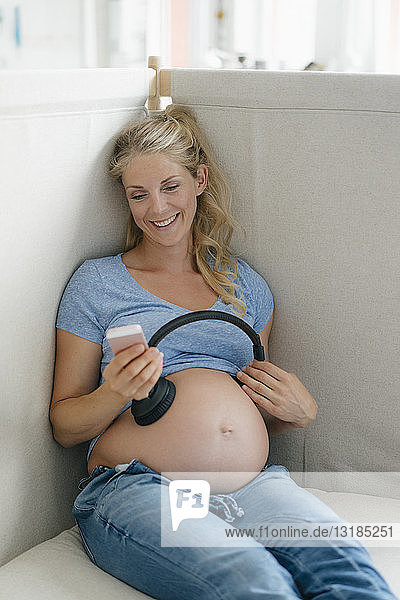 Lächelnde schwangere Frau hält Kopfhörer an ihren Bauch