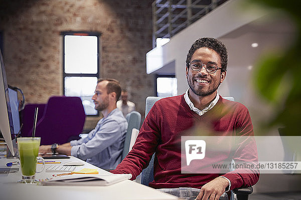 Young man sitting at desk in office  smiling