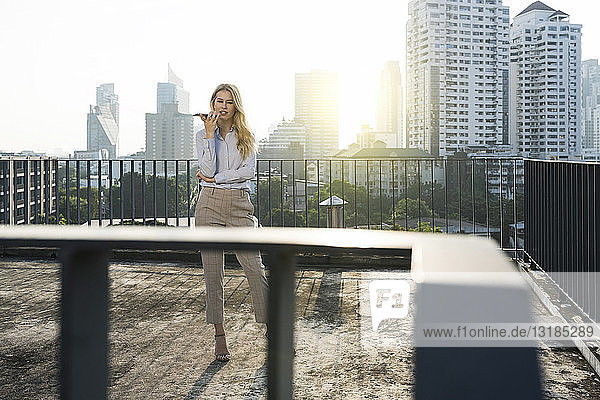 Business woman speaking into smartphone on city rooftop