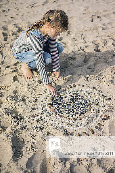 Kleines Mädchen macht am Strand ein Herz aus Muscheln