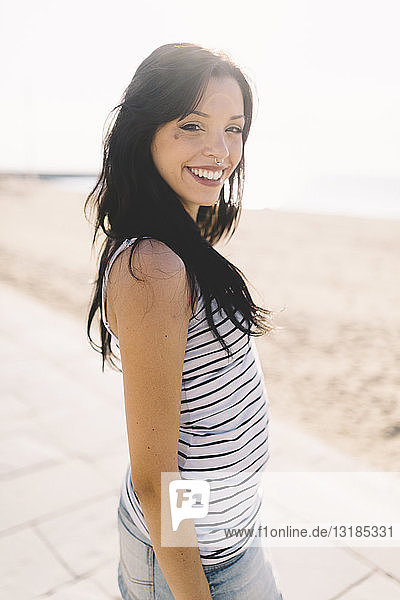 Porträt einer lächelnden jungen Frau mit Nasenpiercing an der Strandpromenade stehend