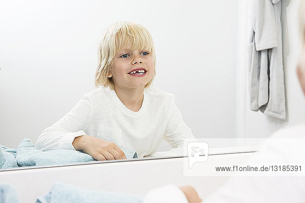 Lächelnder Junge mit Zahnlücke beim Blick in den Badezimmerspiegel