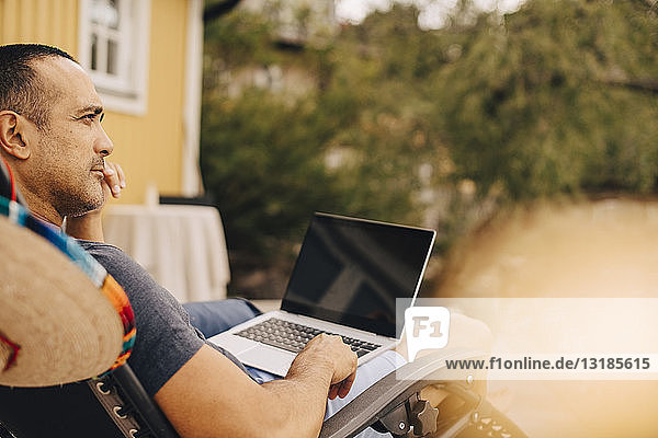 Nachdenklicher Mann benutzt Laptop  während er im Sommer in einer Ferienvilla sitzt