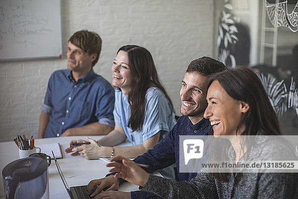 Creative business professionals smiling while sitting at conference table in board room