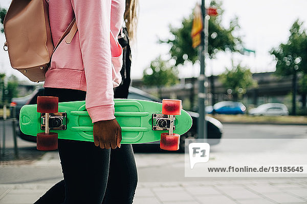 Junge Frau mit grünem Skateboard in der Hand beim Spaziergang in der Stadt