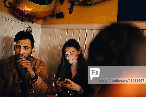 Junge Frau benutzt ein Smartphone  während sie im Restaurant neben einem Mann sitzt