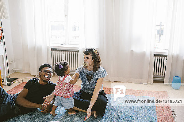 Glückliche Mutter und Vater mit Tochter auf Teppich zu Hause