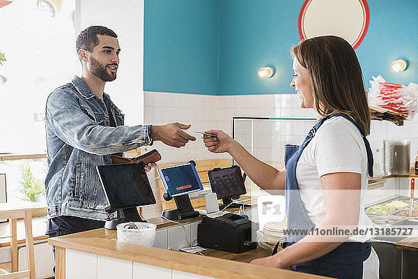 Junge Besitzerin gibt einem männlichen Kunden an der Kasse im Restaurant eine Kreditkarte