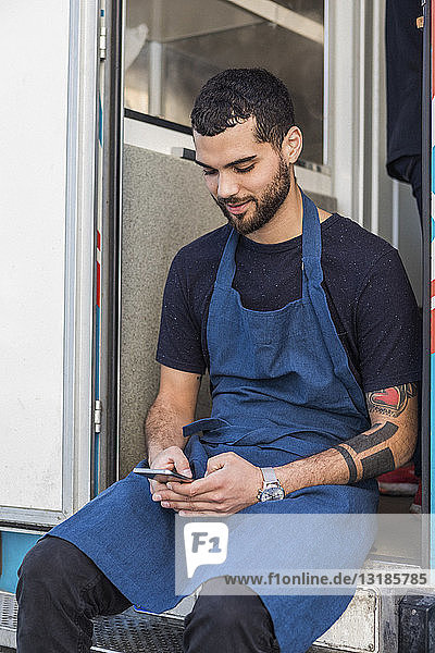 Junger männlicher Unternehmer verschickt Textnachrichten  während er am Eingang eines Speisewagens sitzt