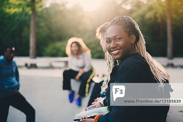 Porträt eines lächelnden Teenagers  der mit Freunden im Skateboard-Park sitzt