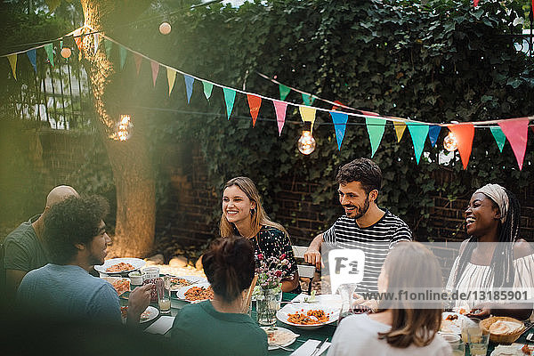 Junge multiethnische Freunde genießen das Abendessen bei Tisch während einer Gartenparty