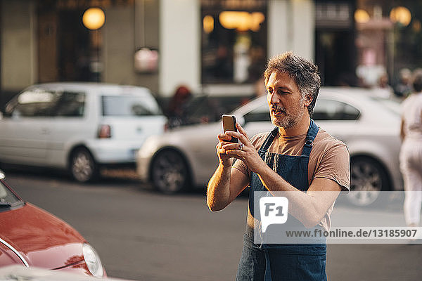 Reifere männliche Besitzer fotografieren mit Mobiltelefon  während sie auf der Straße stehen