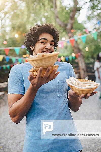 Smiling young man carrying food in bowls during dinner party in backyard