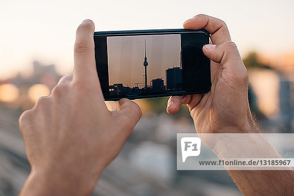 Cropped image of young man photographing Fernsehturm through smart phone during sunset