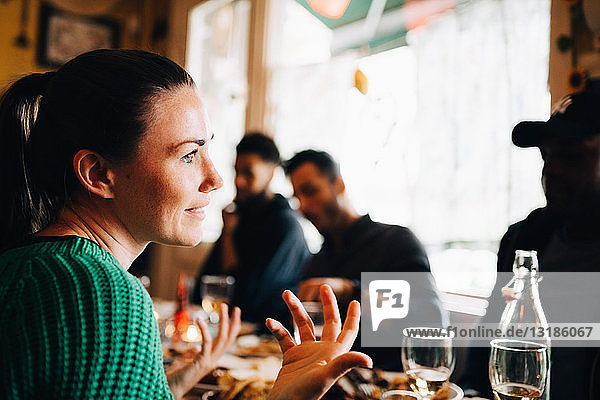Smiling young woman gesturing while sitting in restaurant during brunch party