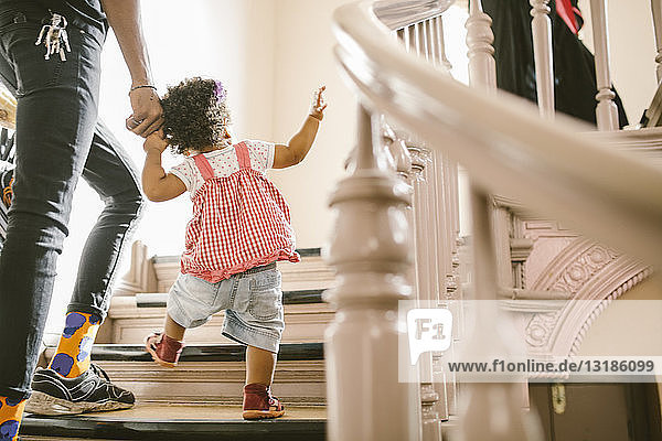 Kleines Mädchen hält Hand des Vaters beim Treppensteigen in Wohnung