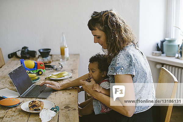 Frau  die ihre Tochter mit Essen füttert  während sie im Haus am Esstisch sitzt