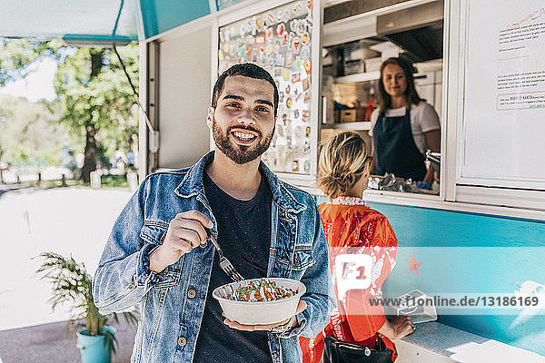 Portrait of smiling young man eating fresh Tex-Mex in bowl against food truck