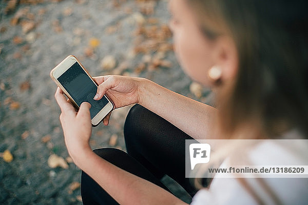 Hochwinkelaufnahme einer jungen Frau  die ein Mobiltelefon benutzt  während sie auf einem Fußweg sitzt