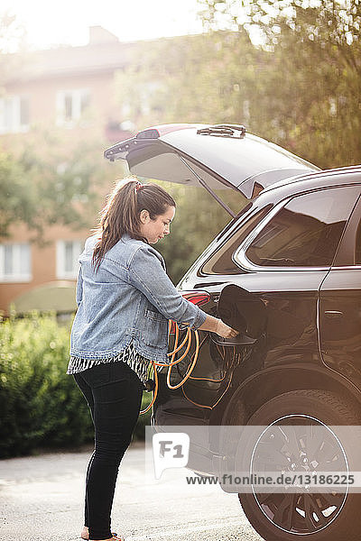 Seitenansicht einer Frau  die ein Elektroauto auf der Auffahrt auflädt