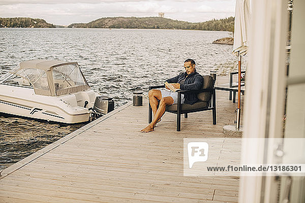 Ein Mann liest in voller Länge ein Buch  während er auf der Terrasse am See sitzt