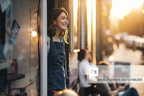 Smiling female owner looking away while standing at entrance of deli