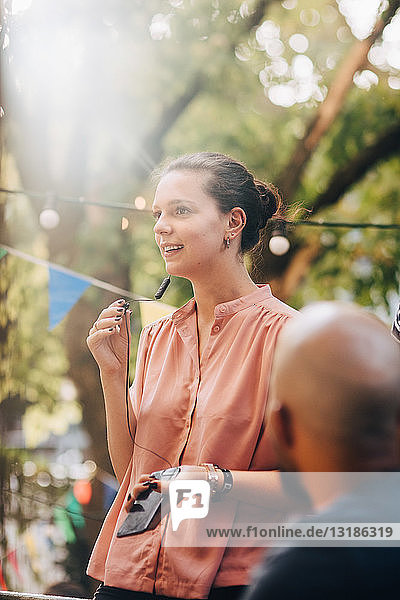 Young woman looking away while talking through earphones in balcony during party
