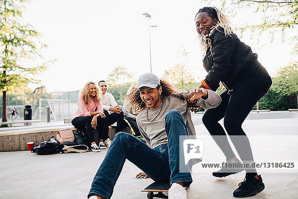 Teenager drängt glücklichen Mann auf Skateboard beim Spielen im Park