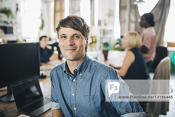 Portrait of confident businessman sitting at desk in creative office