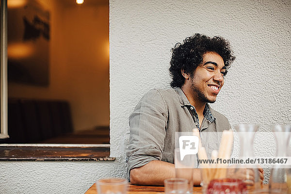 Smiling young man looking away while sitting at table against wall