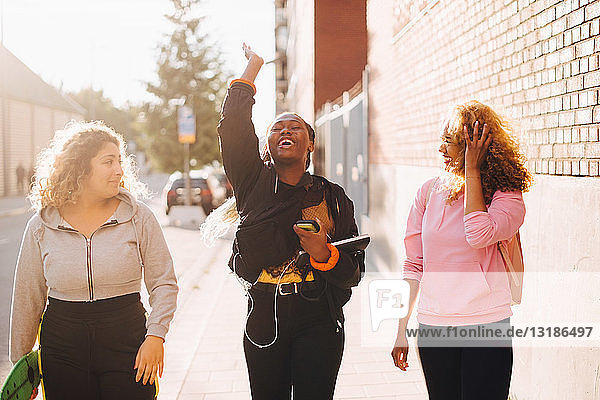 Fröhliche Frau spricht mit Freunden  während sie in der Stadt auf dem Bürgersteig geht