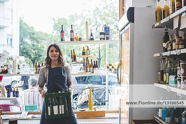 Porträt einer selbstbewussten Mitarbeiterin  die im Feinkostladen Flaschen in Kisten trägt