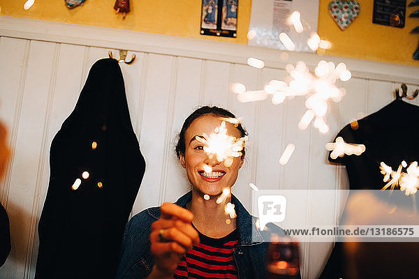 Fröhliche junge Frau mit Wunderkerze in der Hand während einer Dinnerparty im Restaurant