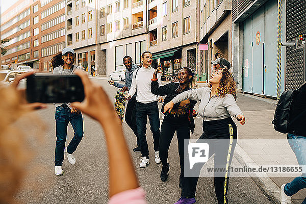 Woman photographing friends dancing on street in city