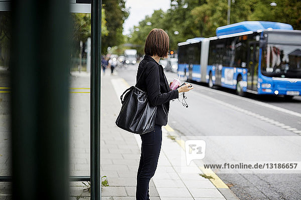 Seitenansicht einer Geschäftsfrau  die auf dem Bürgersteig steht und an einer Bushaltestelle in der Stadt wartet