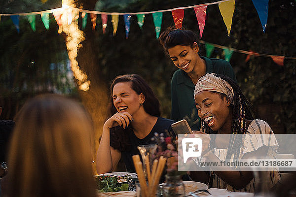 Cheerful multi-ethnic friends enjoying at table during dinner party in backyard