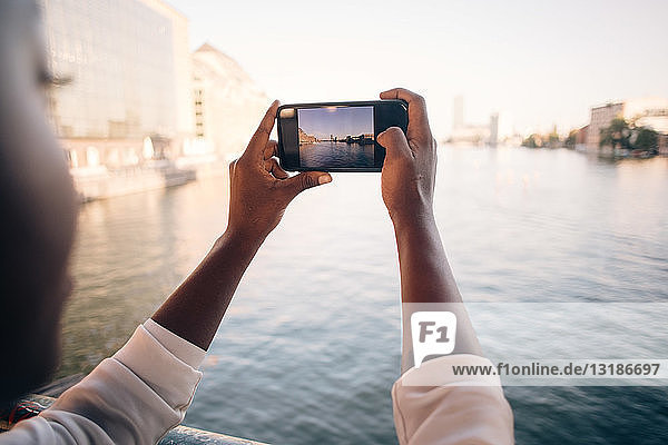 Ausschnitt einer jungen Frau  die in der Stadt mit ihrem Handy einen Fluss fotografiert